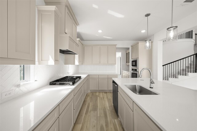 kitchen with appliances with stainless steel finishes, decorative backsplash, light hardwood / wood-style floors, pendant lighting, and sink