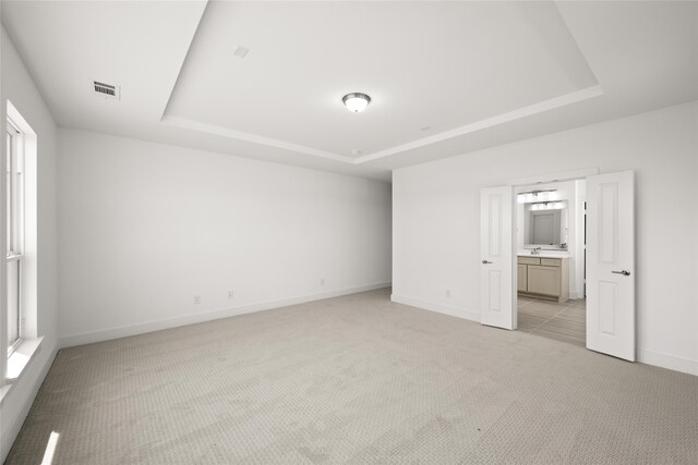 unfurnished bedroom with light colored carpet, a raised ceiling, ensuite bath, and sink