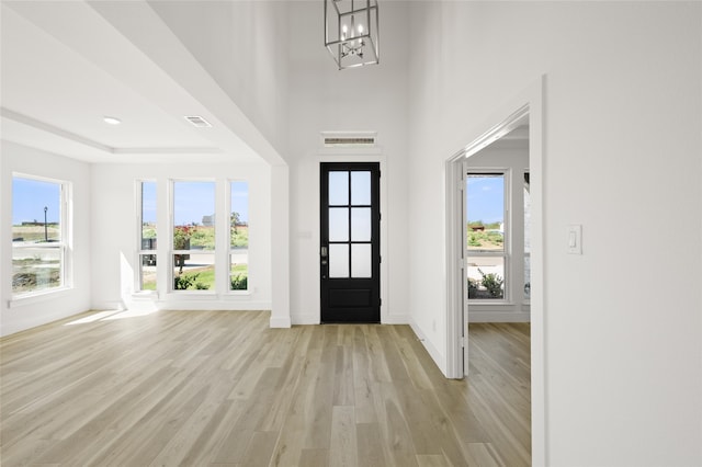 entryway with light wood-type flooring, a chandelier, a raised ceiling, and plenty of natural light