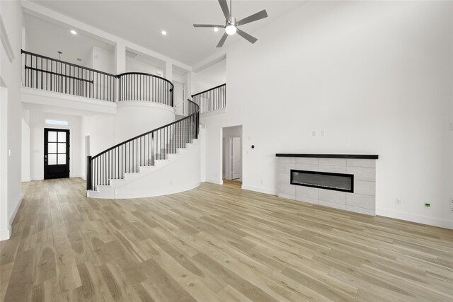 unfurnished living room with a high ceiling, a fireplace, ceiling fan, and light hardwood / wood-style flooring