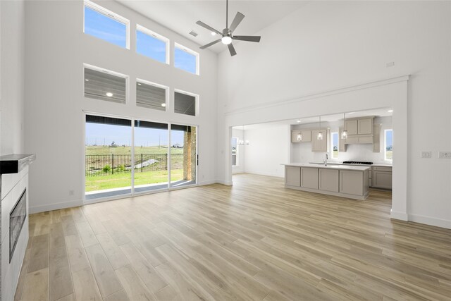 unfurnished living room featuring a high ceiling, light hardwood / wood-style floors, ceiling fan, and sink