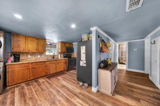 kitchen with stainless steel appliances, ornamental molding, wood-type flooring, sink, and stacked washer / drying machine