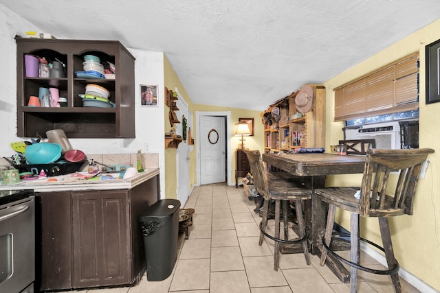 kitchen with light tile flooring, stove, dark brown cabinets, a textured ceiling, and lofted ceiling