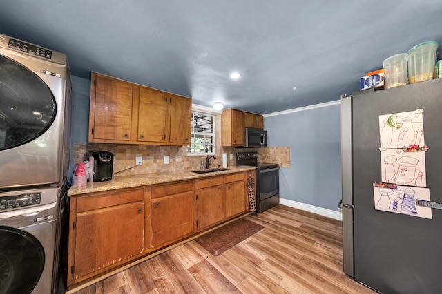 kitchen with backsplash, light wood-type flooring, appliances with stainless steel finishes, sink, and stacked washer / drying machine