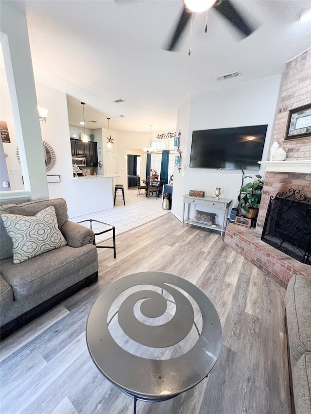 living room with a fireplace, brick wall, ceiling fan with notable chandelier, and hardwood / wood-style floors