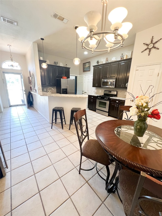 kitchen featuring kitchen peninsula, decorative light fixtures, light tile flooring, an inviting chandelier, and appliances with stainless steel finishes