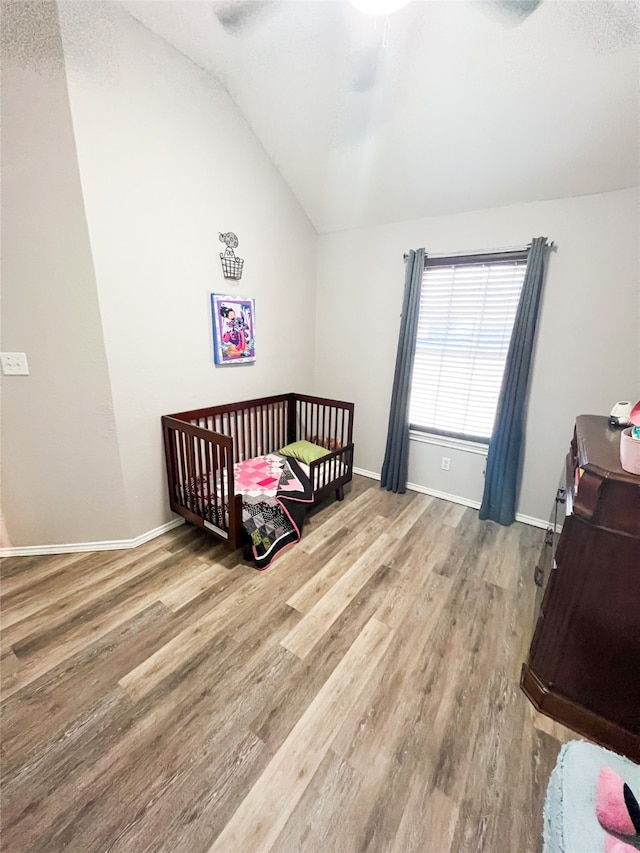 bedroom featuring a crib, ceiling fan, vaulted ceiling, and wood-type flooring