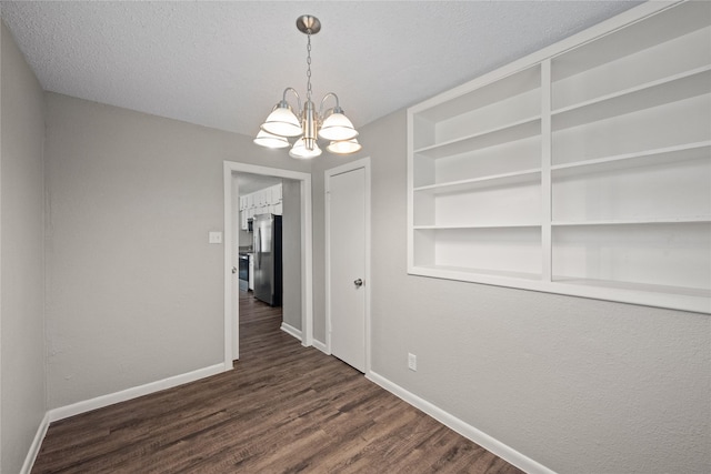 unfurnished dining area with built in features, a textured ceiling, dark hardwood / wood-style flooring, and an inviting chandelier