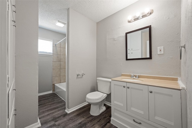 full bathroom featuring vanity, hardwood / wood-style flooring, tiled shower / bath combo, toilet, and a textured ceiling