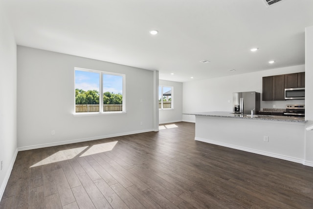 kitchen featuring baseboards, dark wood-style flooring, light stone countertops, stainless steel appliances, and dark brown cabinets