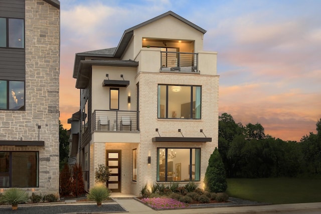 modern home with a balcony, stucco siding, and brick siding