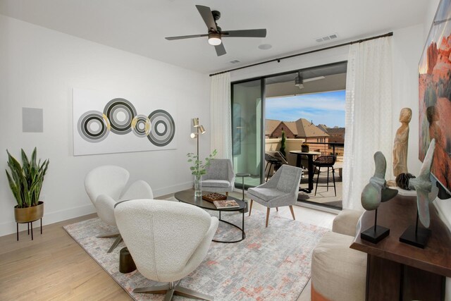 living area with a ceiling fan, wood finished floors, visible vents, and baseboards