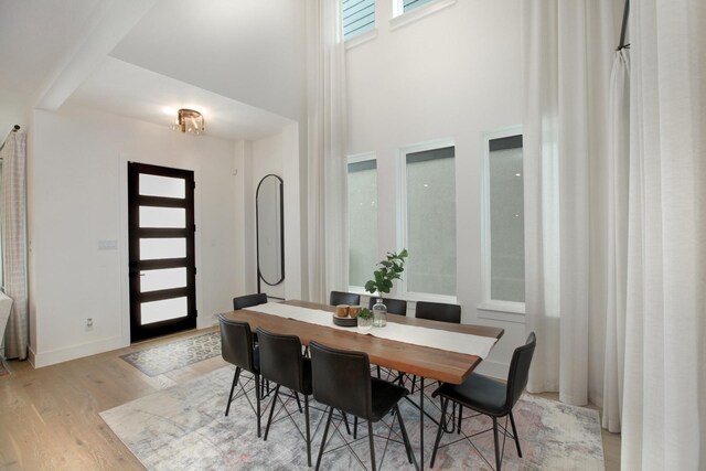 dining room featuring a towering ceiling, light wood-style floors, and baseboards