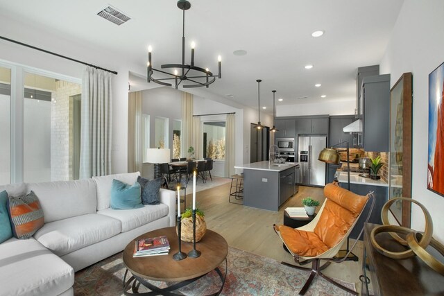 living room featuring a chandelier, light wood-type flooring, visible vents, and recessed lighting