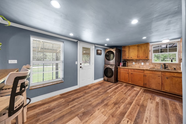 kitchen featuring sink, stacked washing maching and dryer, hardwood / wood-style floors, and backsplash