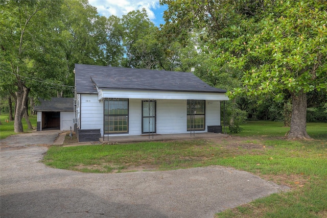 view of front of property featuring aphalt driveway, a porch, an outbuilding, and a front yard