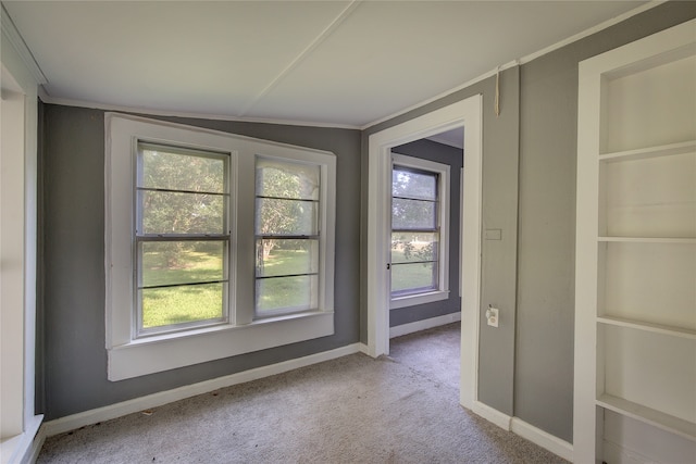 carpeted spare room with lofted ceiling, built in features, ornamental molding, and a healthy amount of sunlight