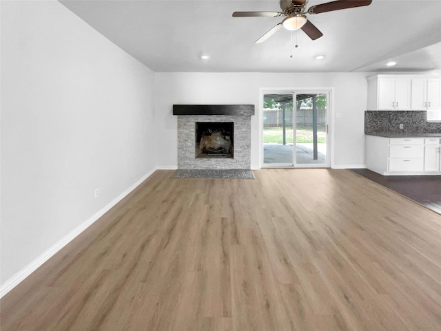 unfurnished living room with a stone fireplace, ceiling fan, and light hardwood / wood-style flooring