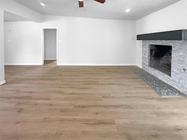 unfurnished living room with ceiling fan, a stone fireplace, and light hardwood / wood-style floors