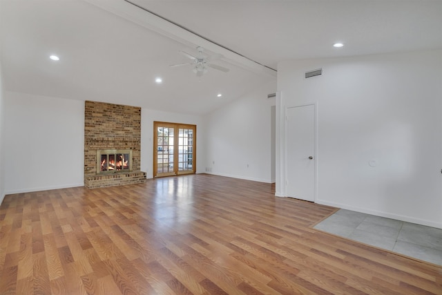 unfurnished living room with brick wall, light hardwood / wood-style flooring, a fireplace, ceiling fan, and vaulted ceiling with beams