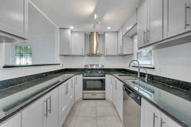 kitchen with dark stone counters, light tile floors, wall chimney range hood, sink, and appliances with stainless steel finishes