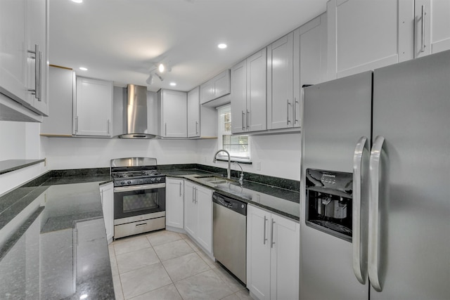 kitchen with white cabinetry, dark stone countertops, stainless steel appliances, wall chimney exhaust hood, and sink