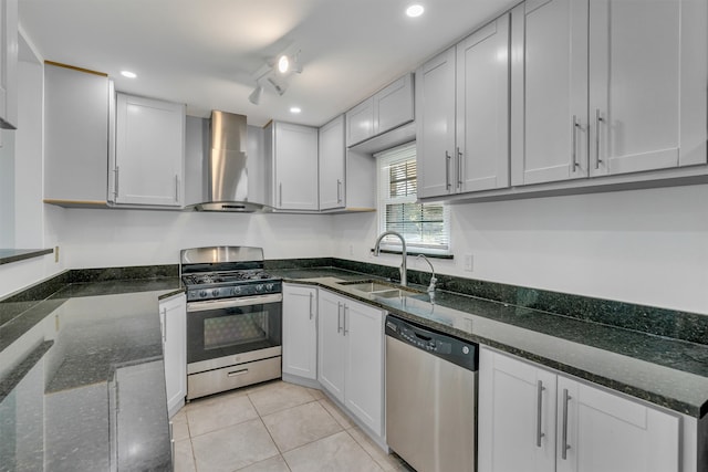 kitchen featuring appliances with stainless steel finishes, wall chimney exhaust hood, sink, track lighting, and light tile floors