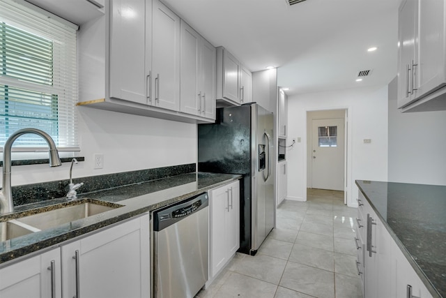 kitchen with white cabinetry, dark stone countertops, appliances with stainless steel finishes, sink, and light tile floors