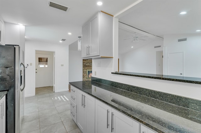 kitchen featuring ceiling fan, a fireplace, stainless steel refrigerator with ice dispenser, light tile floors, and white cabinets