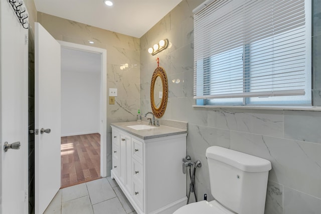 bathroom with tile flooring, vanity, toilet, and tile walls