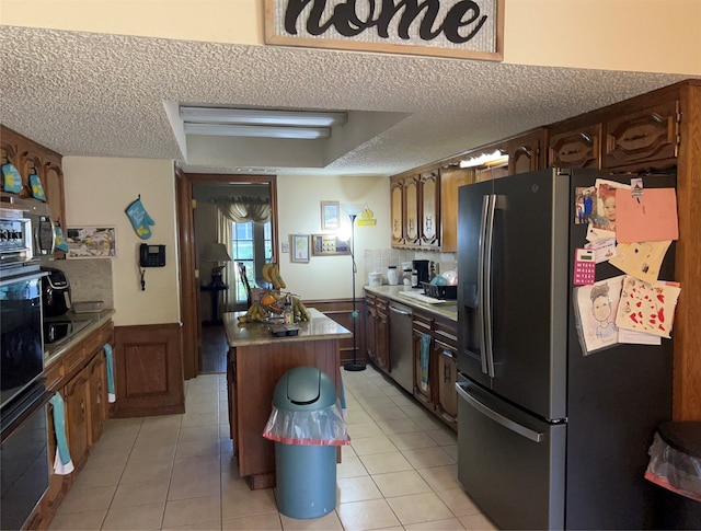 kitchen with a textured ceiling, a kitchen island, light tile floors, and stainless steel appliances