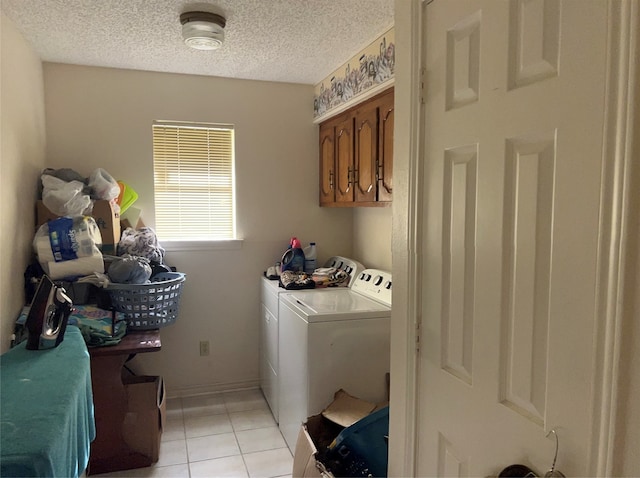 laundry room with cabinets, a textured ceiling, light tile flooring, and washer and clothes dryer