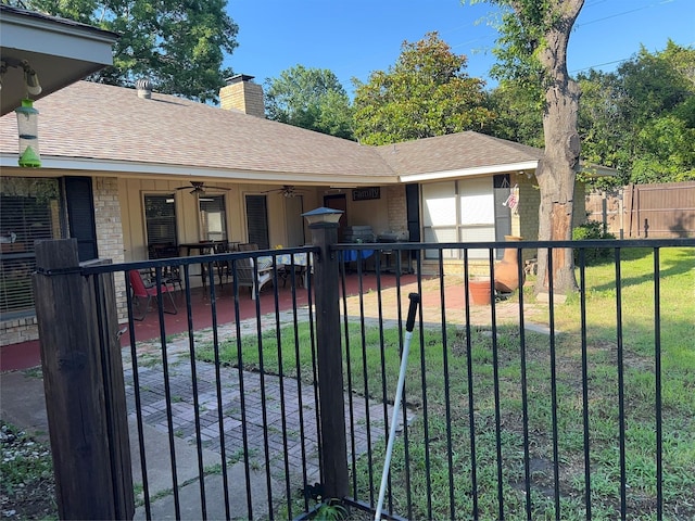 view of front facade featuring fence, a ceiling fan, a shingled roof, a patio area, and brick siding