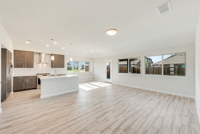 kitchen featuring a kitchen island with sink, backsplash, light hardwood / wood-style flooring, and wall chimney range hood