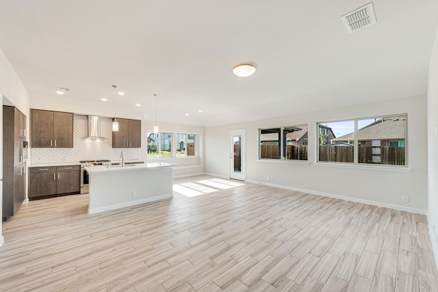 kitchen featuring visible vents, open floor plan, wall chimney range hood, stainless steel range with gas cooktop, and backsplash