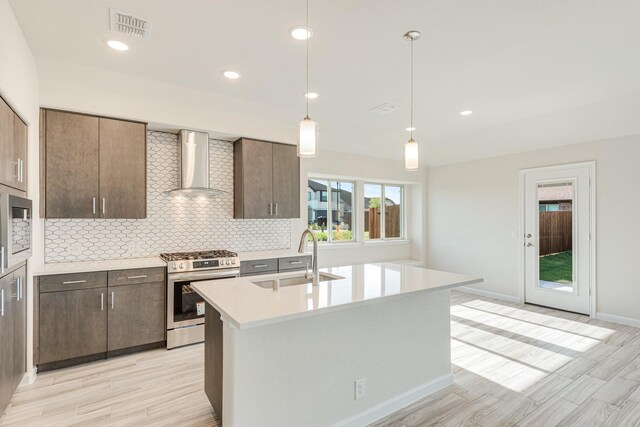 kitchen with stainless steel appliances, wall chimney exhaust hood, tasteful backsplash, sink, and a center island with sink