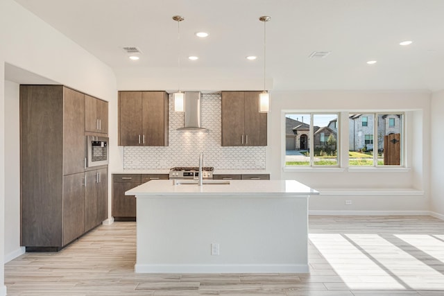 kitchen featuring light wood finished floors, visible vents, light countertops, wall chimney range hood, and backsplash