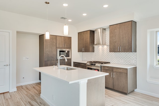 kitchen with decorative backsplash, wall chimney exhaust hood, gas stove, sink, and a center island with sink