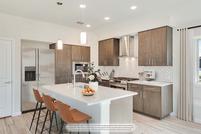 kitchen featuring appliances with stainless steel finishes, tasteful backsplash, sink, a center island with sink, and wall chimney range hood