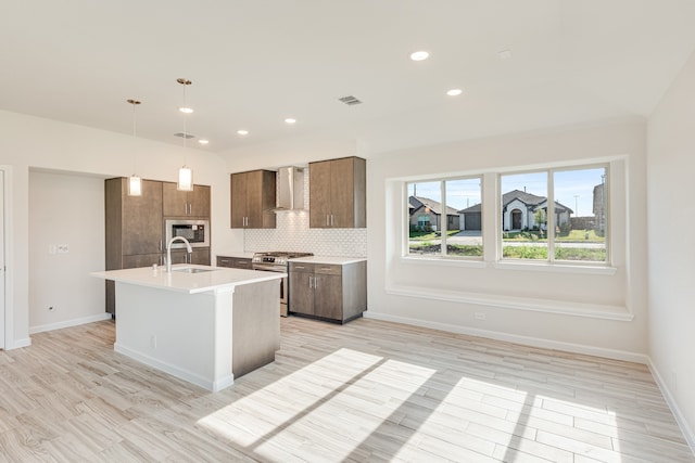 kitchen with wall chimney exhaust hood, tasteful backsplash, an island with sink, stainless steel range oven, and decorative light fixtures