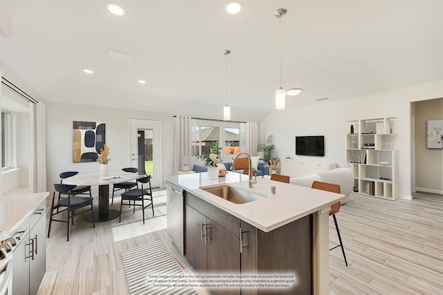 kitchen featuring sink, dark brown cabinets, an island with sink, light hardwood / wood-style floors, and pendant lighting