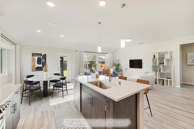 kitchen with a sink, light countertops, light wood-type flooring, pendant lighting, and stainless steel dishwasher