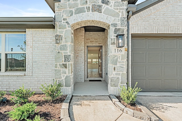 doorway to property with a garage, stone siding, and brick siding