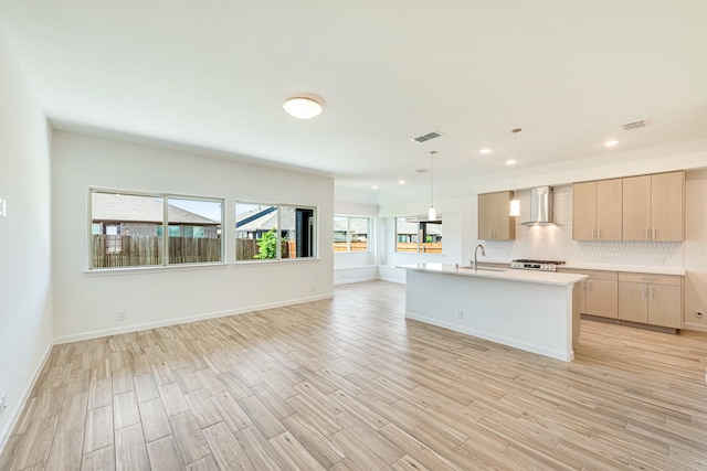 kitchen featuring light wood-style flooring, open floor plan, light countertops, wall chimney range hood, and light brown cabinetry