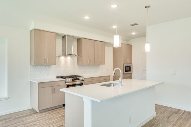 kitchen with sink, decorative backsplash, wall chimney range hood, and an island with sink