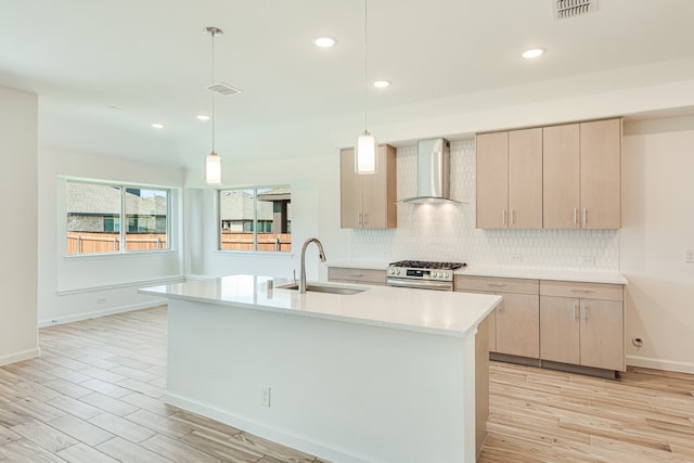 kitchen featuring decorative backsplash, sink, gas stove, wall chimney range hood, and light brown cabinetry