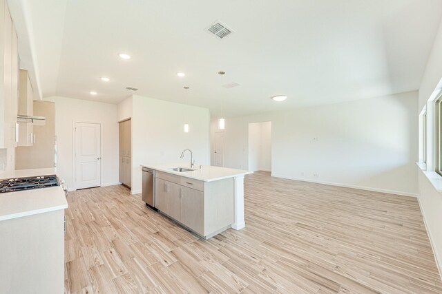 kitchen featuring decorative light fixtures, stainless steel dishwasher, sink, an island with sink, and light wood-type flooring