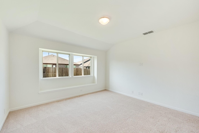 empty room with visible vents, vaulted ceiling, light carpet, and baseboards