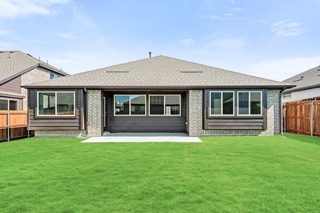 rear view of property with brick siding, a shingled roof, a lawn, a patio area, and fence private yard