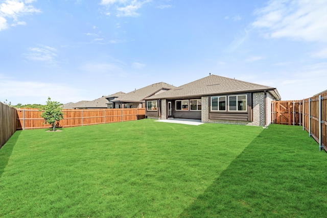 back of house featuring a fenced backyard, brick siding, a yard, roof with shingles, and a patio area